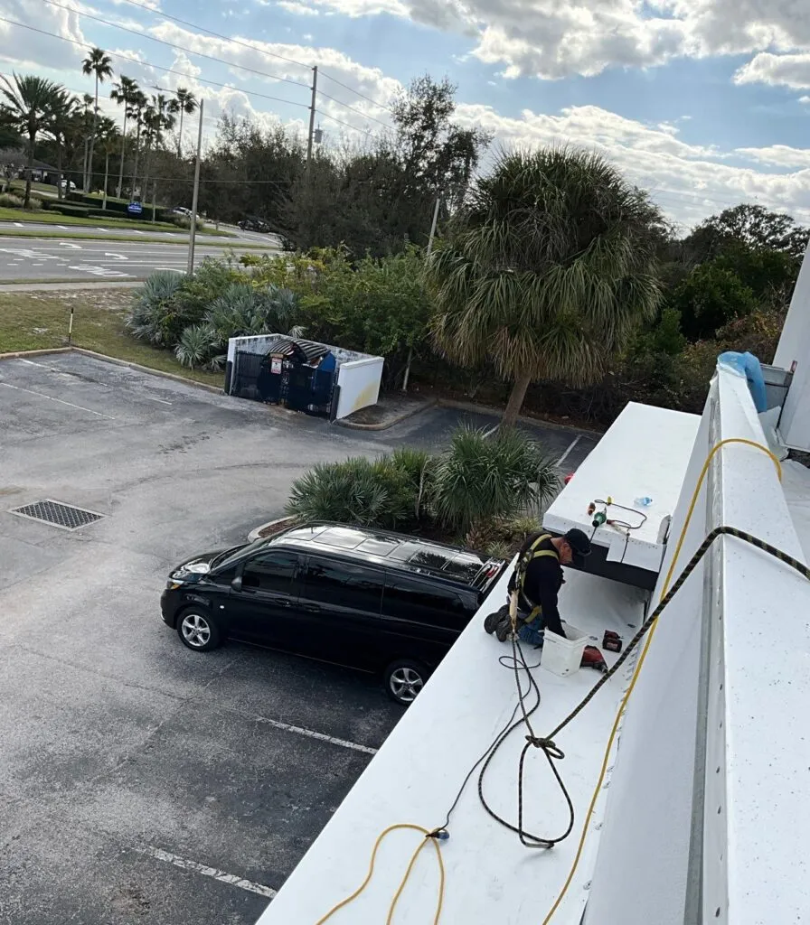 roofer wearing harness on awning of a flat roof working on roof replacement