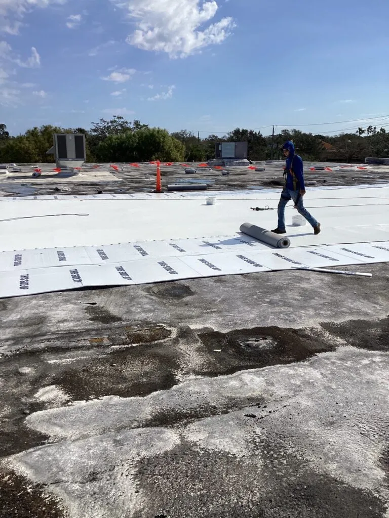 roofer rolling out single-ply roofing on a flat roof during replacement