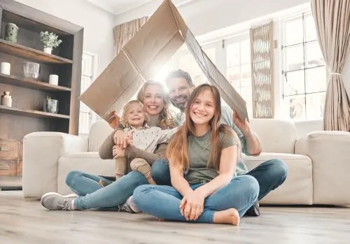 happy family smiling under cardboard box bent to be shaped like a roof